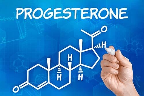 A hand writing on a board with the word progesterone written in it.